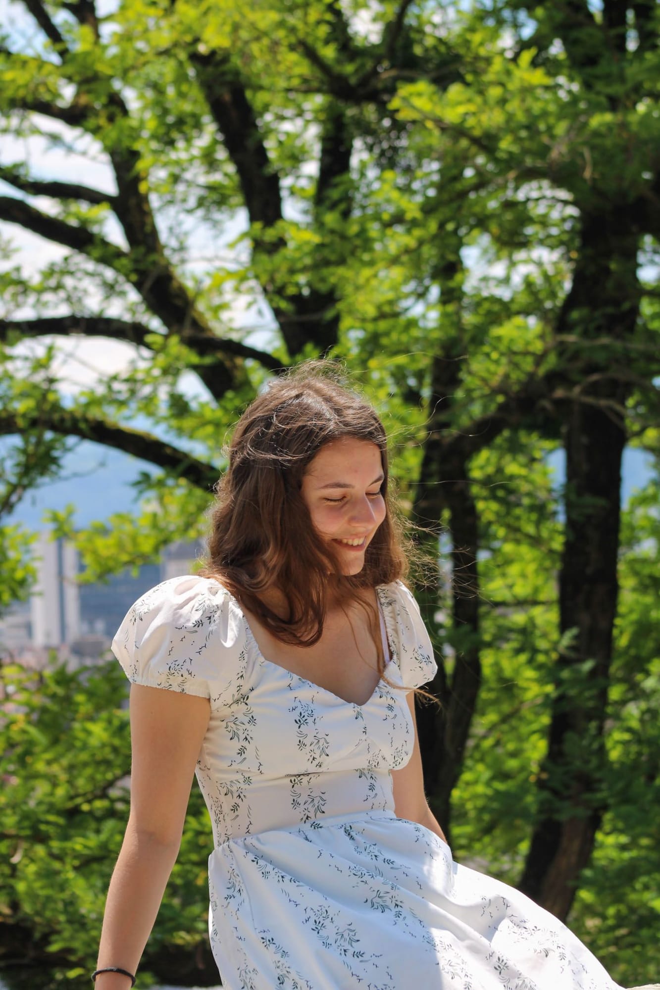 Sourire spontané en robe blanche à motifs sous les grands arbres, photo de mariage naturelle près de Grenoble