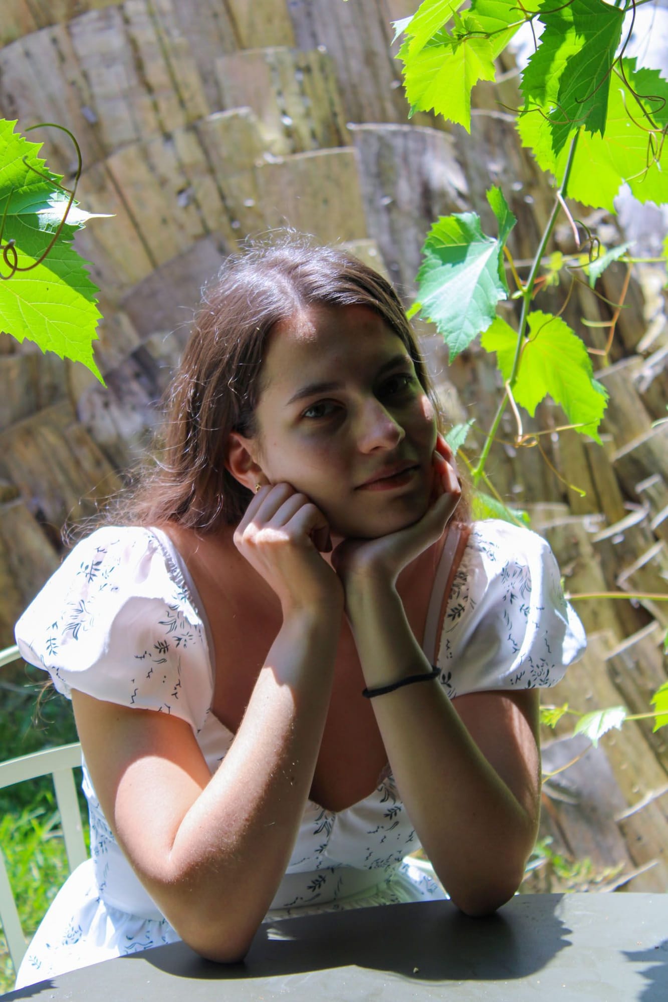Portrait assis sous une treille de vigne, menton posé sur les mains, ambiance champêtre pour un mariage bohème