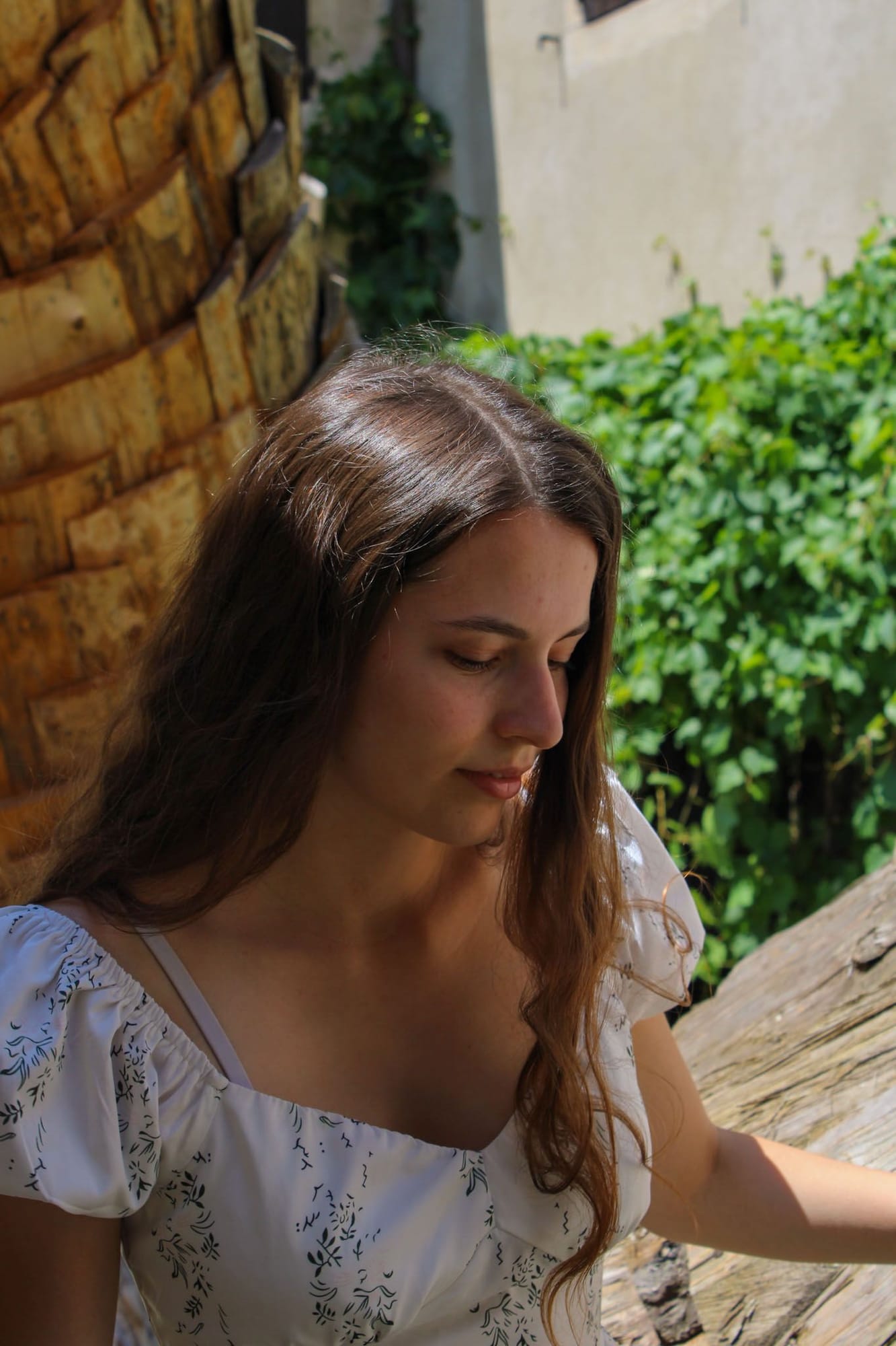 Portrait de profil, regard baissé, robe blanche à manches bouffantes devant un mur de bois et de vigne, photo de mariage douce et intimiste